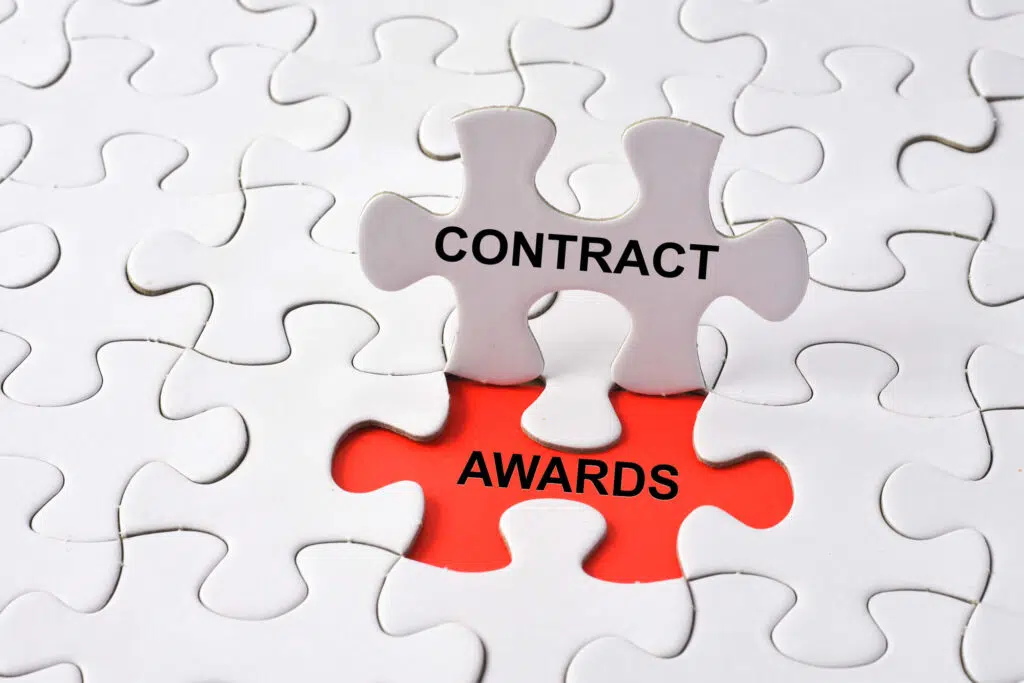A white puzzle with one puzzle piece that says contract standing up revealing the word awards in the empty space