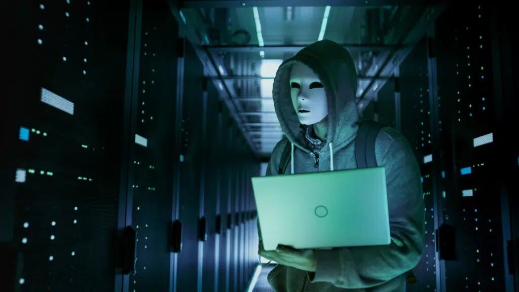 A person wearing a mask and holding a laptop